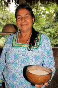 Doña Carmela, a woman from the Ecuadorian Amazon, smiling while holding a traditional wooden bowl of chicha.
