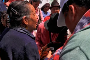 A candid close-up of several people in fedoras and traditional clothing inspecting a rooster at a crowded Ecuadorian market.