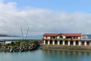 The historic yellow and red Boatshed building on the Wellington waterfront under a cloudy sky with the harbour in the background.