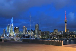 Night view of Auckland skyline featuring the illuminated Sky Tower and the blue neon lights of the Wynyard Crossing bridge.