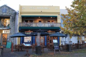 he yellow facade of Póg Mahones Irish Pub in Queenstown with outdoor seating, umbrellas, and autumn leaves on the ground.