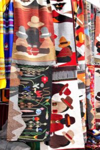 Hand-woven Andean tapestries featuring colorful figures, llamas, and mountain landscapes in Otavalo.