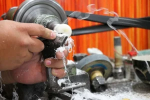Close-up of a craftsman's hands using a lathe to carve a hard white Tagua nut into a polished shape